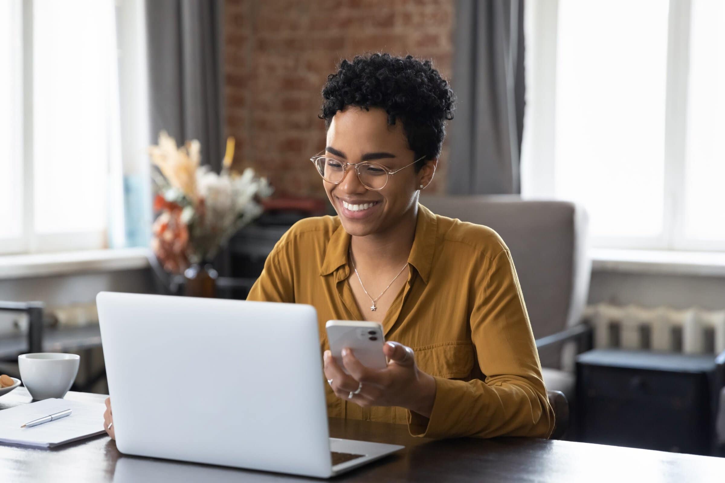 African,Woman,Sit,At,Workplace,Desk,Holds,Cellphone,Staring,At